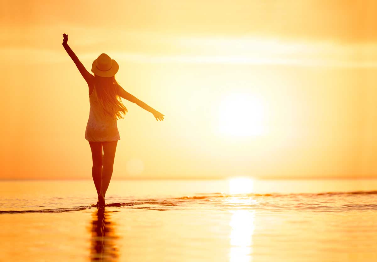Woman walking on beach at golden hour, representing freedom and healing for survivors of human trafficking.